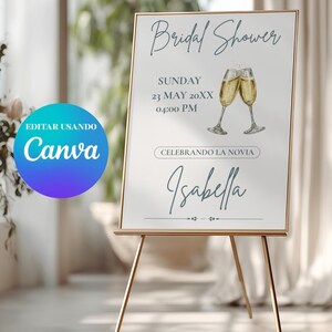 K&ouml;nnte beinhalten: Ein goldgerahmtes Schild auf einer goldenen Staffelei k&uuml;ndigt eine Brautparty an. Das Schild zeigt die Worte "Bridal Shower", Datum, Uhrzeit und den Namen "Isabella". Zwei Champagnergl&auml;ser sind abgebildet. Das Canva-Logo ist sichtbar.