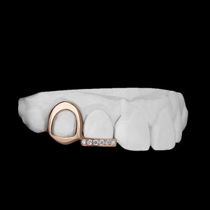 May include: A gold tooth grill with a diamond-encrusted bar. The grill is designed to fit over two teeth and has a curved shape.