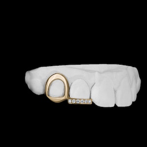 Puede incluir: Grill dental de oro con una barra engastada con diamantes. El grill tiene forma de rectángulo redondeado con un círculo más pequeño en el interior. El grill se muestra en un modelo de boca.