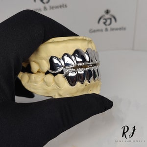 May include: A silver grill with a row of diamonds set in the front. The grill is displayed on a plaster mold of a mouth.