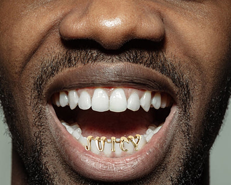 May include: A close-up of a person's mouth with gold teeth that spell out the word "JUICY".