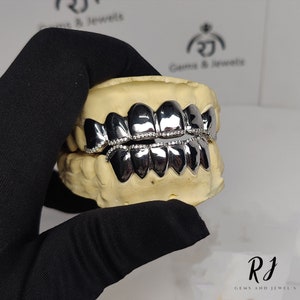 May include: A silver grill with a row of small diamonds around the edge. The grill is displayed in a dental mold.