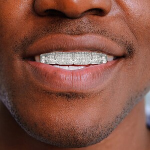 May include: Close-up of a person's mouth with a silver grill, showing a row of sparkling diamonds.