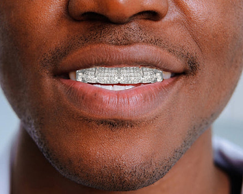 May include: Close-up of a person's mouth with a silver grill, showing a row of sparkling diamonds.