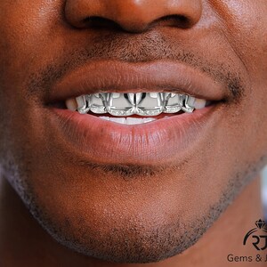 May include: Close-up of a person's mouth with a silver grill featuring a diamond pattern. The grill is made of metal and has a shiny finish.