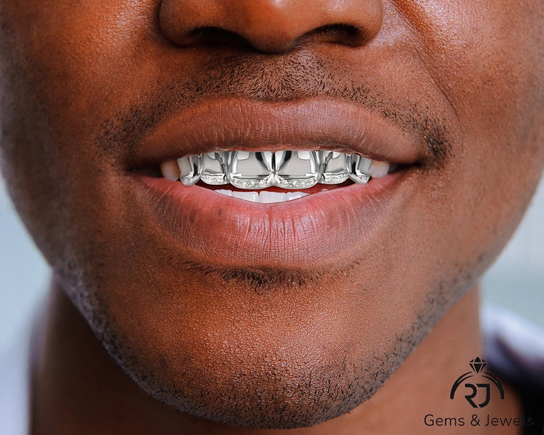May include: Close-up of a person's mouth with a silver grill featuring a diamond pattern. The grill is made of metal and has a shiny finish.