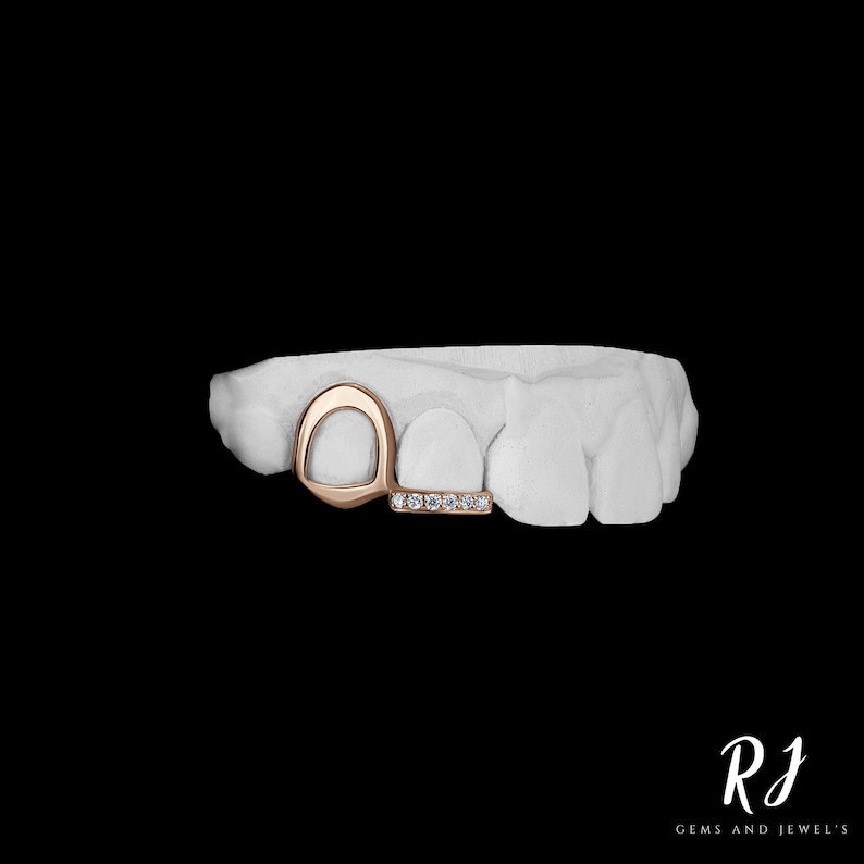 May include: A gold tooth grill with a diamond-encrusted bar. The grill is designed to fit over two teeth and has a curved shape.