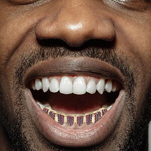 May include: A close-up of a person's mouth with a gold grill with red jewels. The person is smiling and showing their teeth.