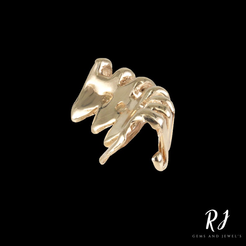 May include: Gold-toned abstract ear cuff with a unique, organic design. The cuff is made of metal and has a curved shape.