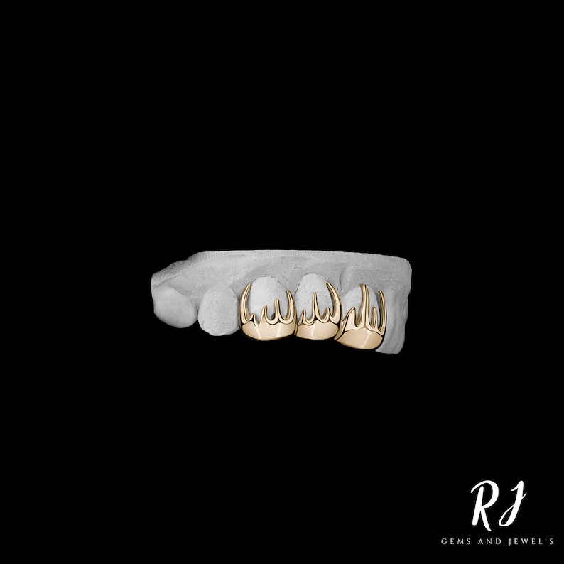 May include: Gold grill with a pointed design, featuring three teeth with multiple points. The grill is displayed on a white mold.