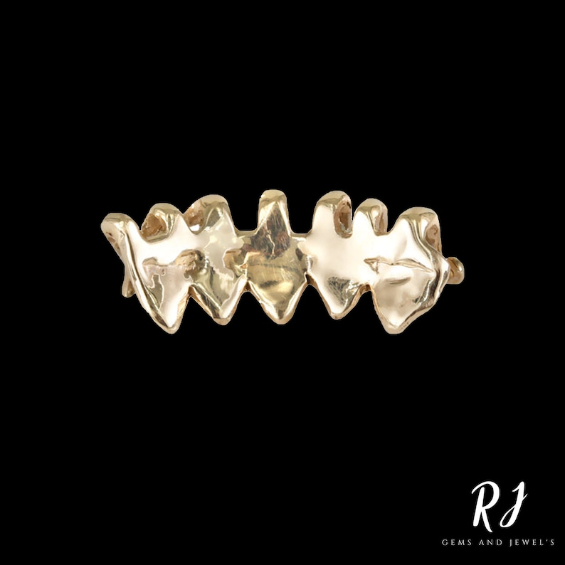 May include: A gold ring with a unique, textured design. The ring is made up of a series of connected, pointed shapes that resemble teeth.