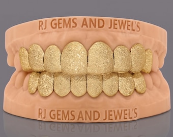 May include: A set of gold-coloured textured teeth grills fitted onto a light peach-coloured dental mould. The text RJ GEMS AND JEWEL'S is printed in a dark font on both the upper and lower sections of the dental model base.