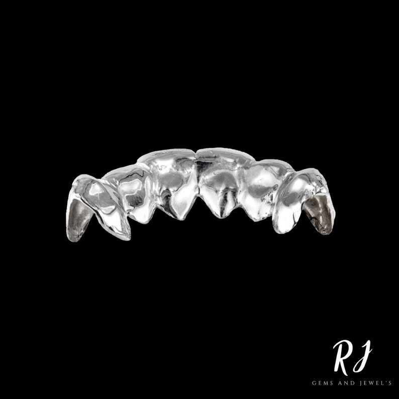 May include: Silver grill with five teeth, designed to fit over the front teeth. The grill is made of a smooth, shiny metal.