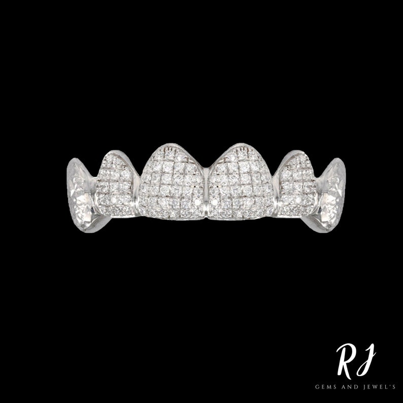 May include: A set of five silver grillz with a diamond-like design. Each grillz is shaped like a tooth and has a row of small, clear stones.