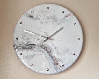 May include: A white and gray marble-effect clock with silver hands and silver accents around the edge.