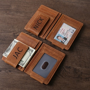 May include: Two brown leather wallets with money clips. The wallets are personalized with the names "JAC" and "NICK".