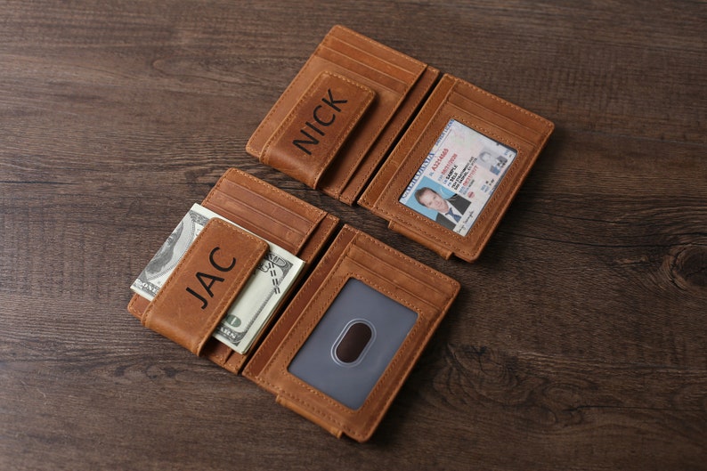 May include: Two brown leather wallets with money clips. The wallets are personalized with the names "JAC" and "NICK".