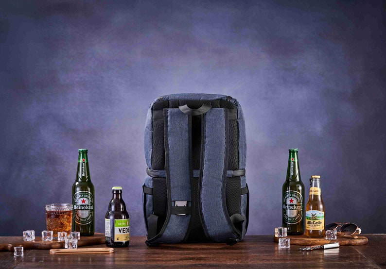May include: A blue insulated backpack with adjustable straps. The backpack is on a wooden table with four bottles of beer and a glass of ice. The bottles are Heineken and Villa Castelli.