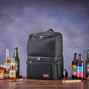 May include: A black insulated backpack cooler with two zippered compartments. The cooler is sitting on a wooden table with various bottles of beer and a glass of ice.