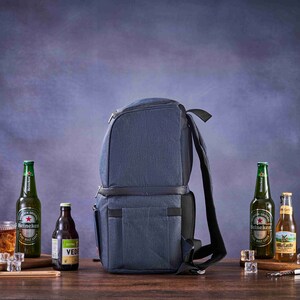 May include: A blue insulated backpack cooler with adjustable straps. The cooler is on a wooden surface with four bottles of beer and a glass of beer.