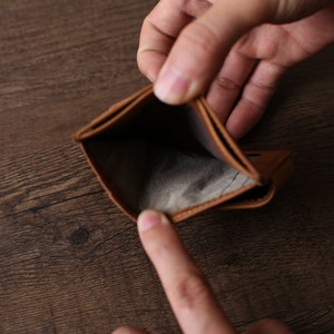 May include: An empty brown leather wallet is held open by two hands. The wallet is completely empty, with no money or cards inside.
