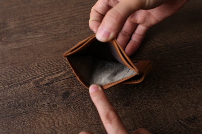 May include: An empty brown leather wallet is held open by two hands. The wallet is completely empty, with no money or cards inside.