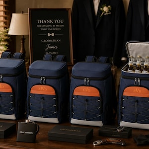 Può includere: Quattro zaini termici blu navy con dettagli arancioni e iniziali personalizzate. Ogni zaino presenta un sistema di cordini elastici frontali, cerniere argentate e una base grigio chiaro. Uno zaino è aperto e mostra quattro bottiglie di vetro all'interno dello scomparto isolato.