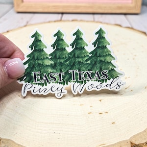 May include: A white sticker with a watercolor illustration of three green pine trees. The text "East Texas Piney Woods" is written in black below the trees.