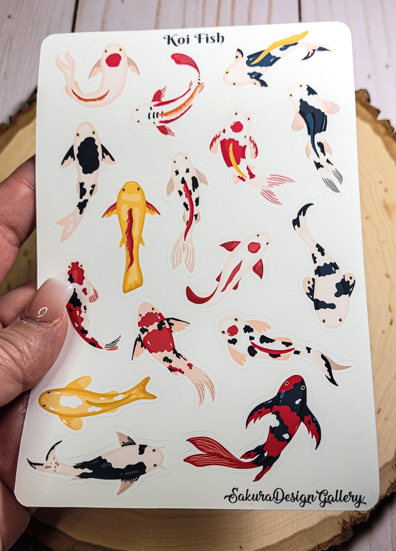 May include: A sheet of stickers featuring 16 colorful koi fish in various poses. The stickers are on a white background with the text "Koi Fish" at the top and "SakuraDesignGallery" at the bottom.