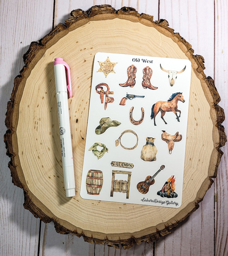 May include: A sheet of stickers with a western theme. The stickers feature images of a sheriff's badge, cowboy boots, a skull, a horse, a cowboy hat, a horseshoe, a lasso, a saddle, a bandana, a barrel, a saloon door, a guitar, and a campfire. The sheet is titled "Old West" and has the text "Sakura Design Gallery" at the bottom.