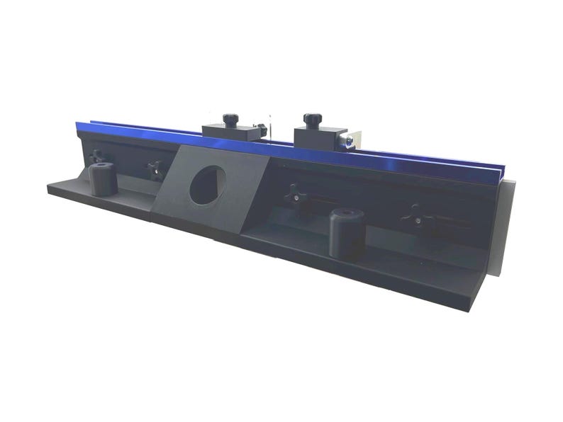 May include: A black and blue metal tool with a rectangular base. The tool has a blue top edge and two black knobs. A circular hole is cut into the center of the tool. The tool is designed for precision work.