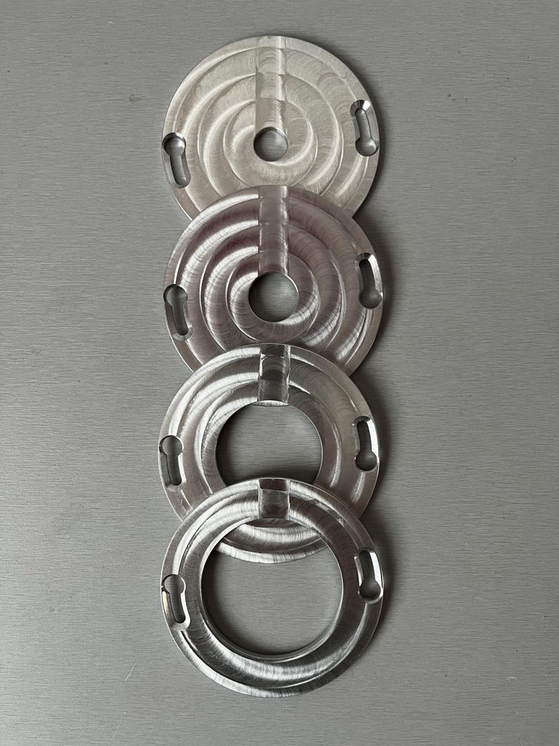 May include: Four silver metal rings with a circular design and a hole in the center. The rings are stacked on top of each other.