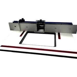 Peut inclure: Une table de toupie blanche avec une bordure noire et rouge. Elle est équipée d'une barrière en métal argenté avec une règle bleue et des boutons de réglage noirs. La table est conçue pour les projets de menuiserie.