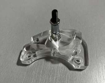 May include: A clear, transparent plastic component with a metal bolt and a silver-colored metal cylinder. The plastic piece has a unique shape with several holes and curved edges. The bolt is black and threaded.