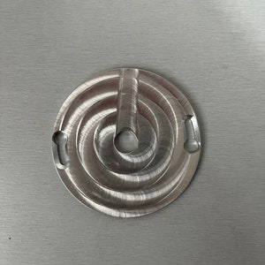 May include: A silver metal circular object with a spiral design and two cutouts on the side. The object has a small hole in the center.