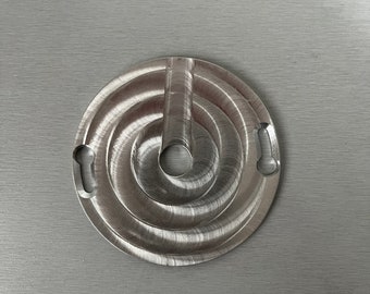 May include: A silver metal circular object with a spiral design and two cutouts on the side. The object has a small hole in the center.