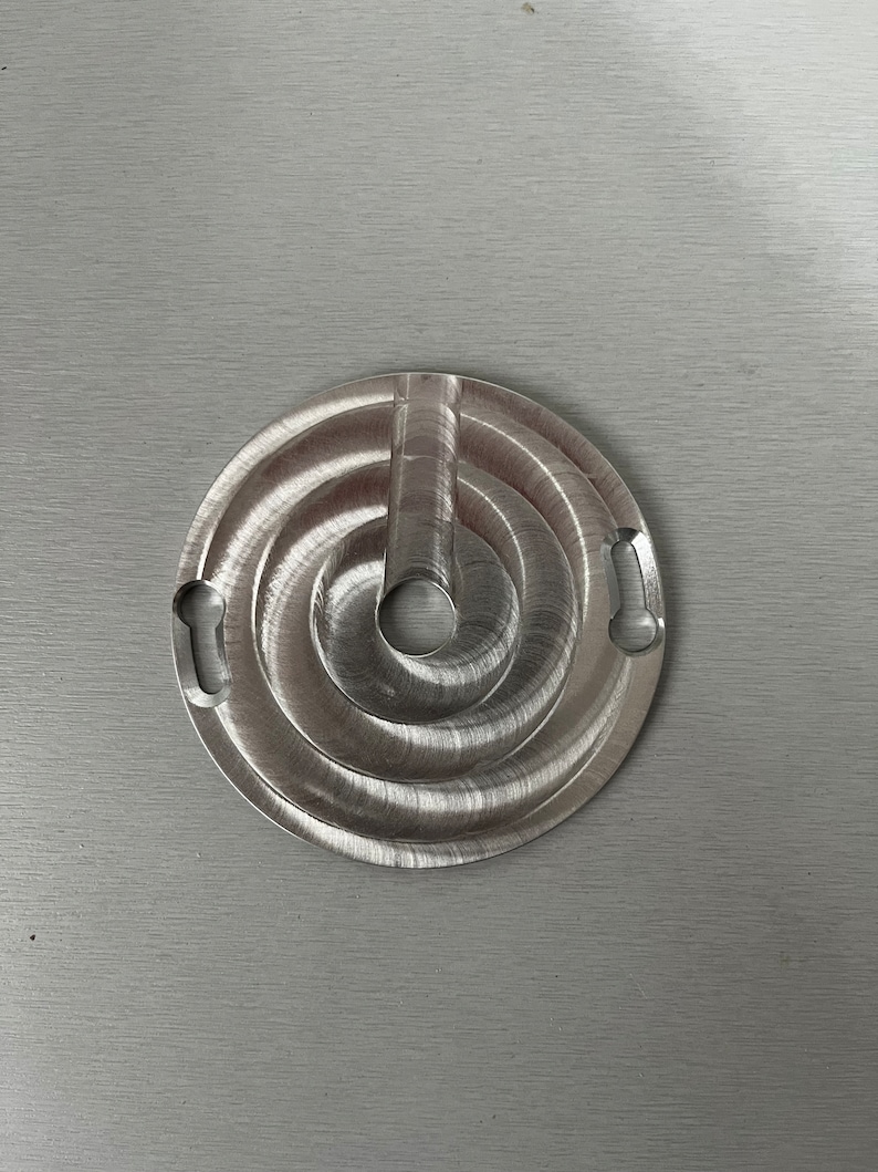 May include: A silver metal circular object with a spiral design and two cutouts on the side. The object has a small hole in the center.