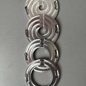 May include: Four silver metal rings with a circular design and a hole in the center. The rings are stacked on top of each other.