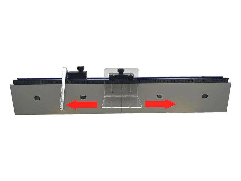 May include: A silver-colored woodworking tool with a black ruler and clear plastic components. The tool has two black knobs and red arrows indicating direction. The tool is designed for precise measurements and cuts.