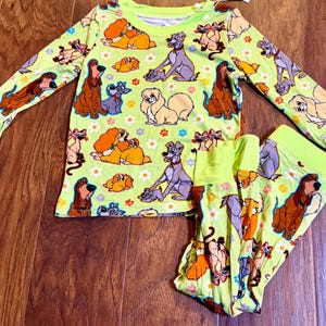 May include: A two-piece pajama set featuring a light green background with a repeating pattern of cartoon dogs and cats. The long-sleeved top and pants have bright green cuffs and hems.