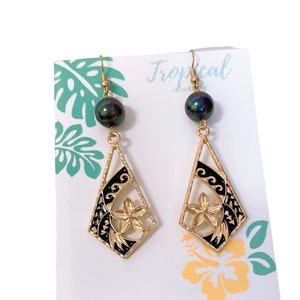 May include: Gold earrings with black and gold floral designs and black pearl accents. The earrings are displayed on a white card with the word "Tropical" printed on it.