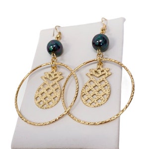 May include: Gold hoop earrings with a pineapple charm and a dark green pearl dangle.
