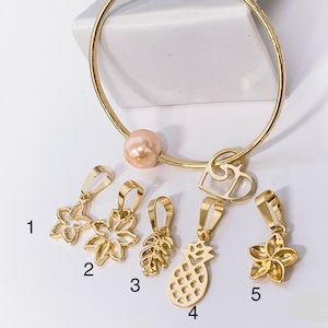 May include: Gold charm bracelet with a pearl bead and five different charms: a flower, a leaf, a pineapple, and two more flowers. The charms are numbered 1 through 5.
