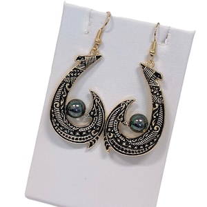 May include: Gold tone earrings with a black and gold fish hook design and a dark green pearl accent.