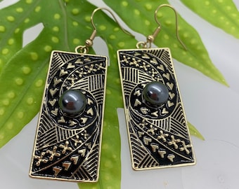 May include: Gold earrings with black and gold geometric designs and a black pearl in the center of each earring.