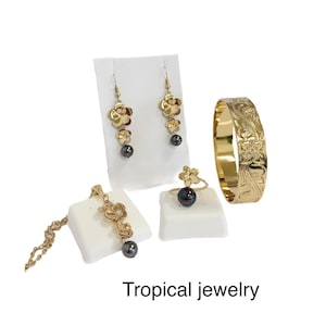 May include: A set of tropical jewelry featuring gold flower designs and black pearls. The set includes a necklace, earrings, a ring, and a bracelet.