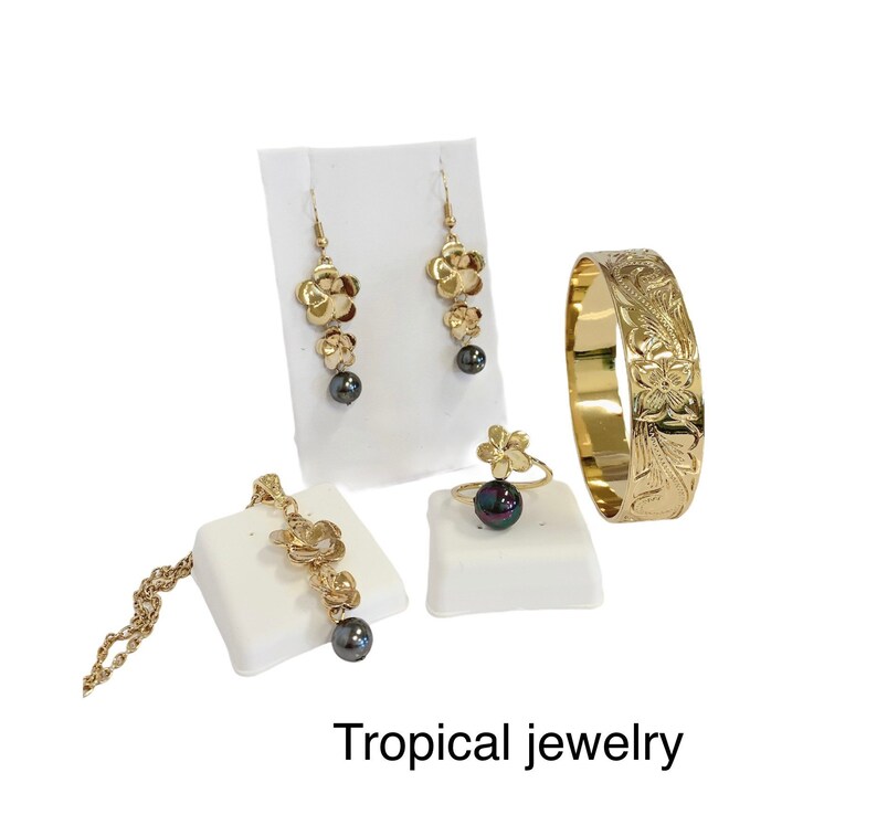 May include: A set of tropical jewelry featuring gold flower designs and black pearls. The set includes a necklace, earrings, a ring, and a bracelet.