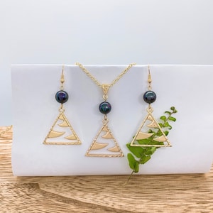 May include: A gold necklace and earrings set with a black pearl pendant and matching earrings. The pendant and earrings feature a triangular design with a textured surface.