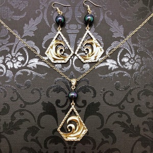 May include: A gold necklace and earrings set with a black pearl pendant and matching earrings. The pendant and earrings feature a wave design.