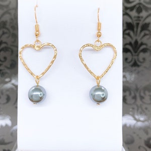 May include: Gold heart-shaped earrings with a dangling gray pearl on each earring.